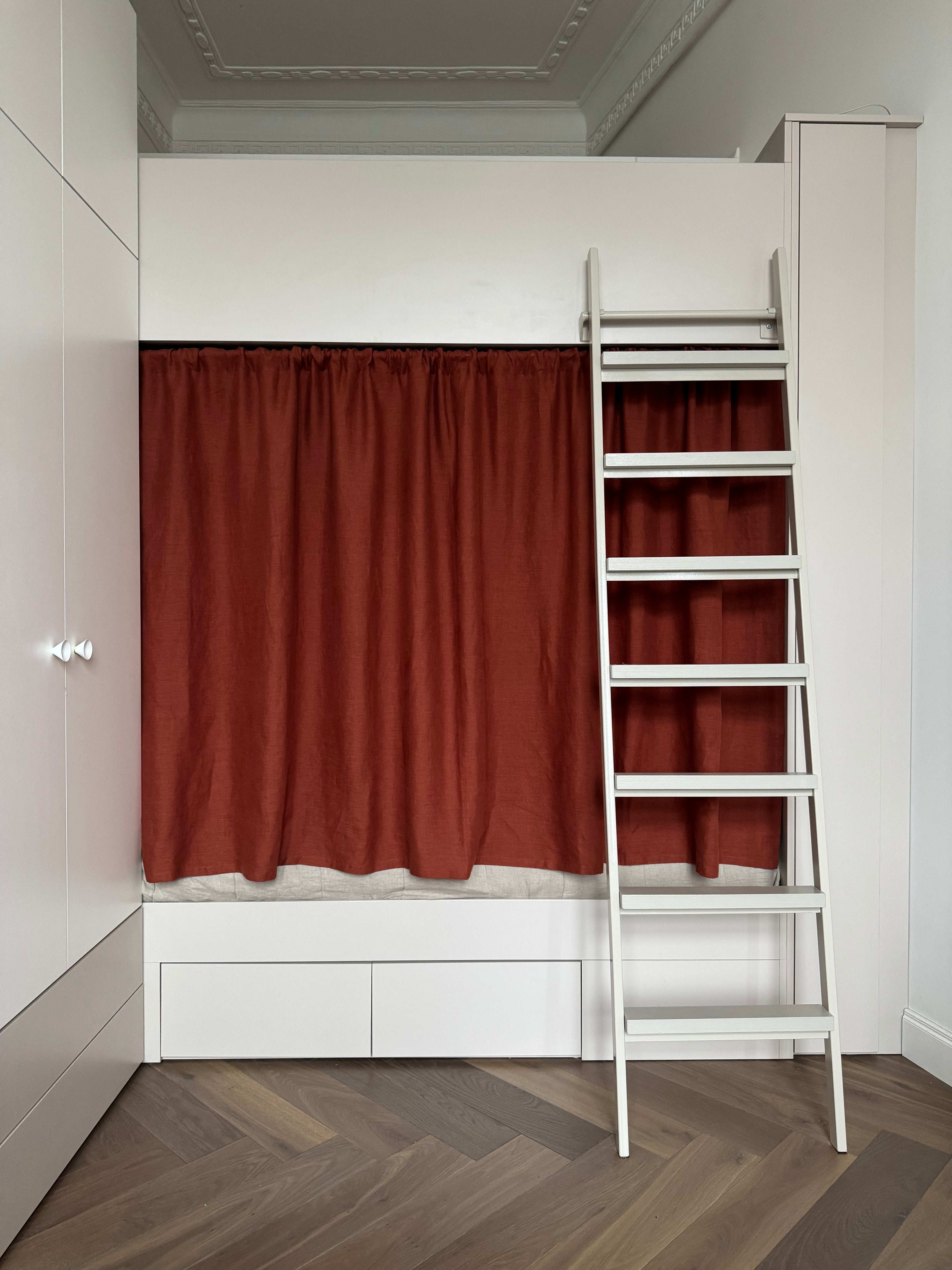 Bunk bed with rust linen curtains and a white ladder in a room with wooden flooring.