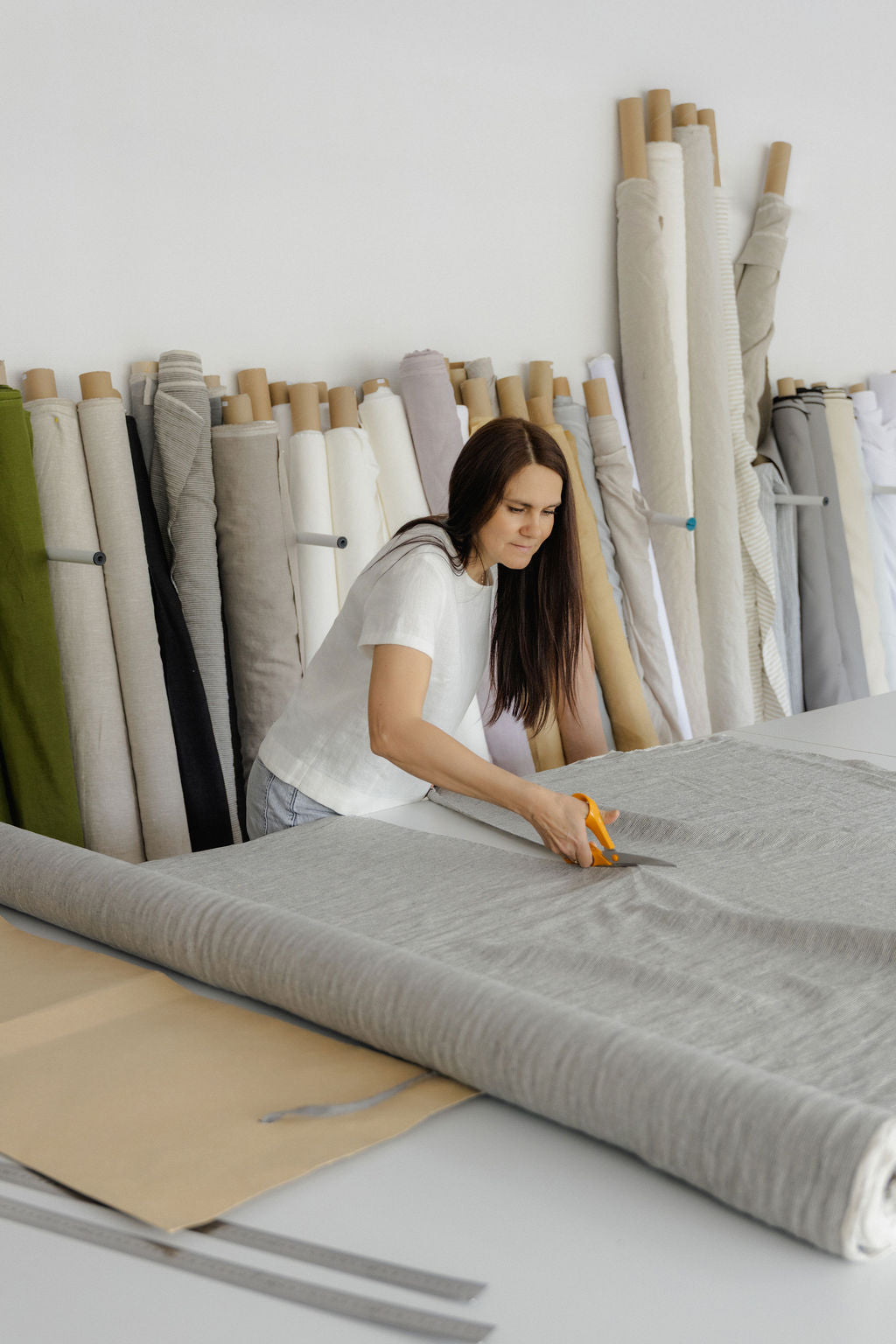 Woman cutting linen fabric in a room with various fabric rolls.
