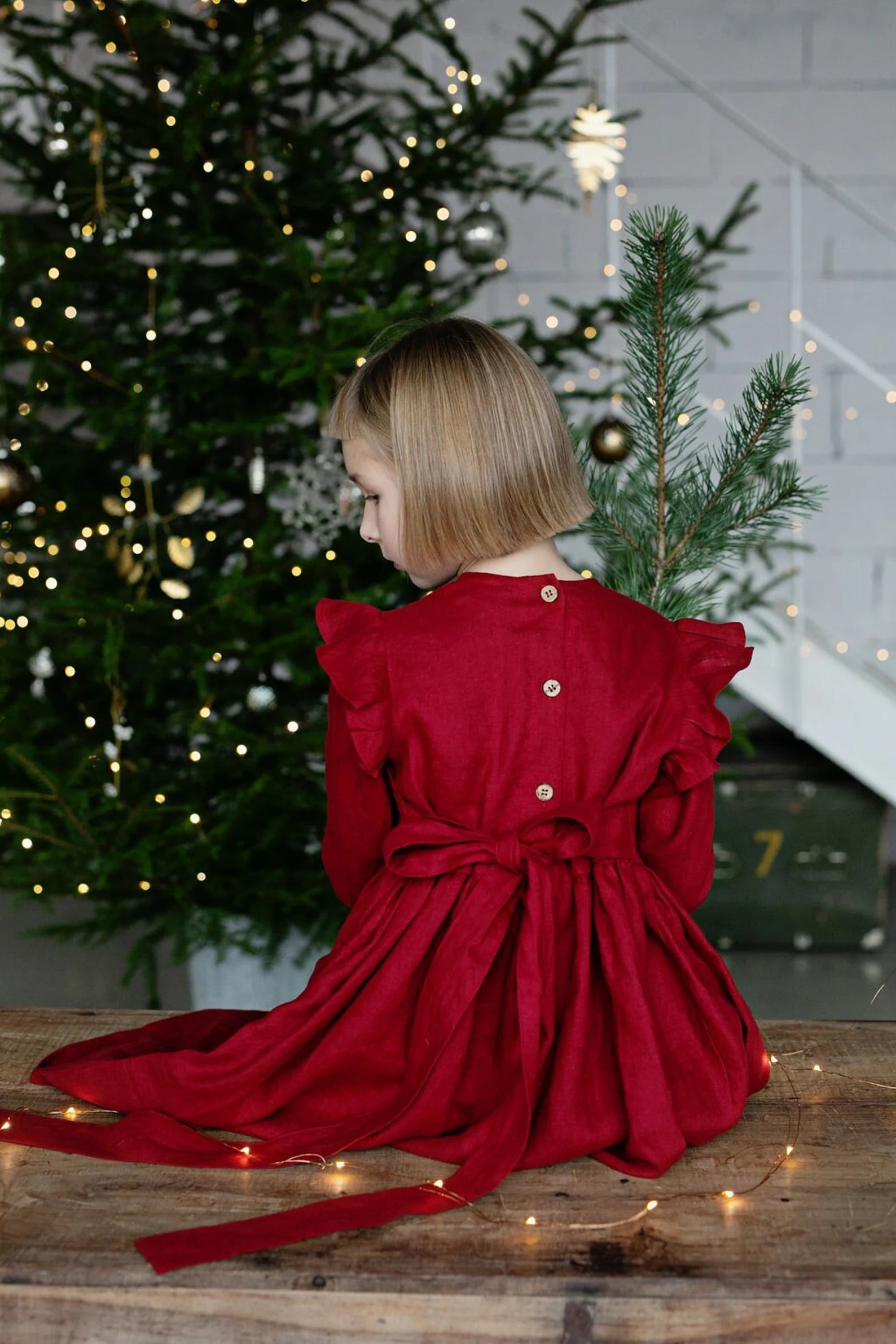 Girl in a red linen dress sitting in front of a decorated Christmas tree.