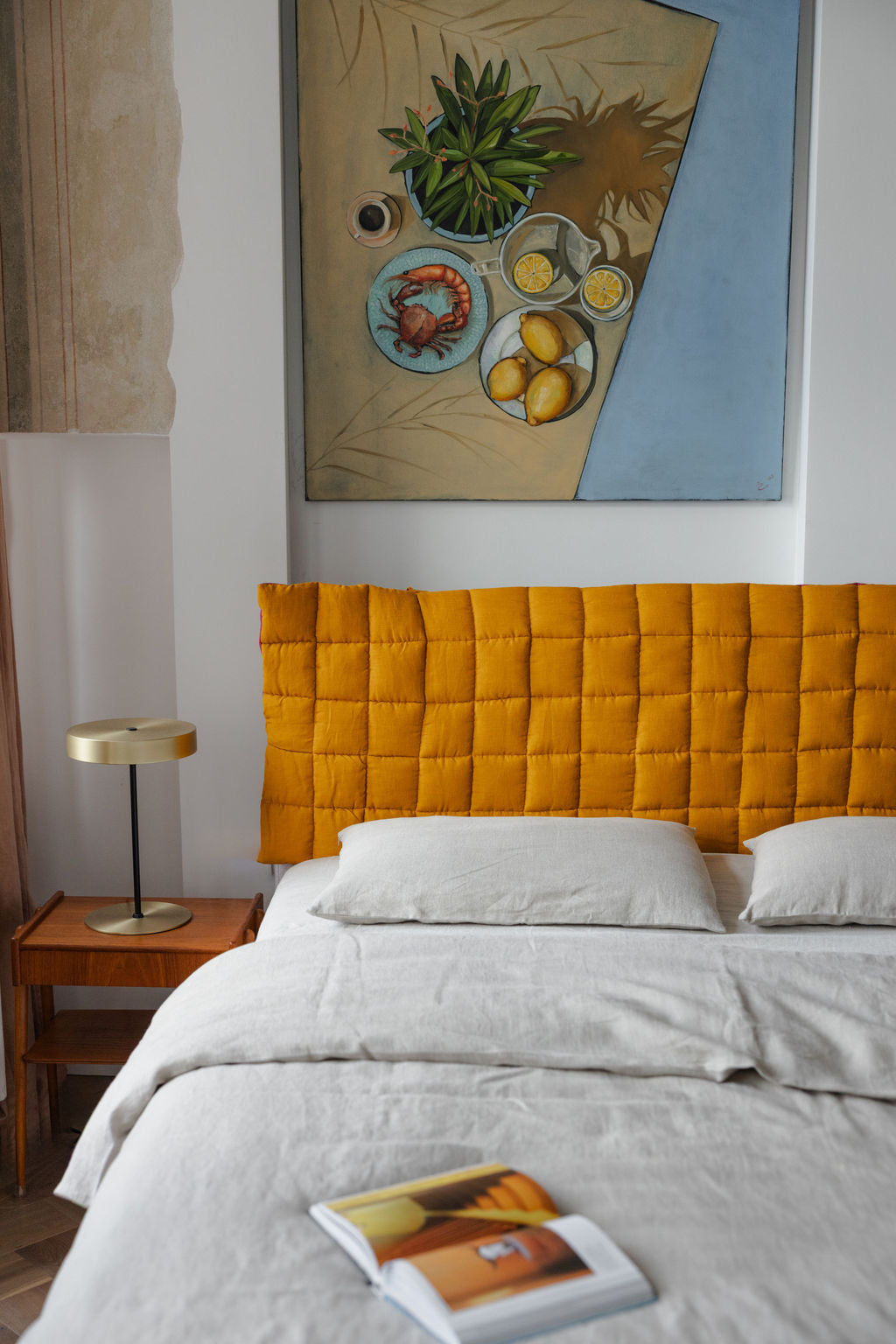 Bedroom with a yellow headboard, white bedding, and a painting on the wall.