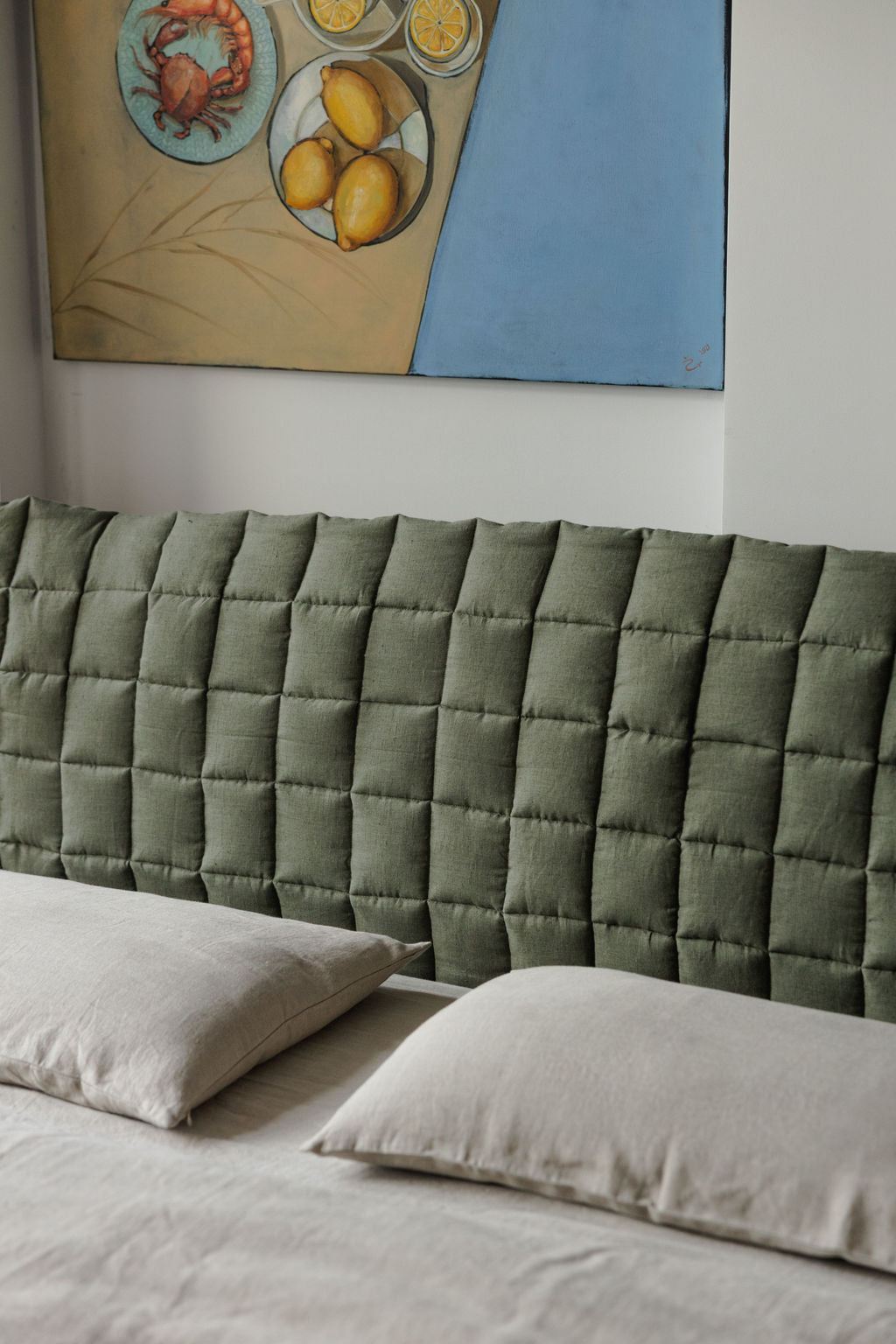 Green tufted headboard with beige pillows against a white wall with a colorful abstract painting.