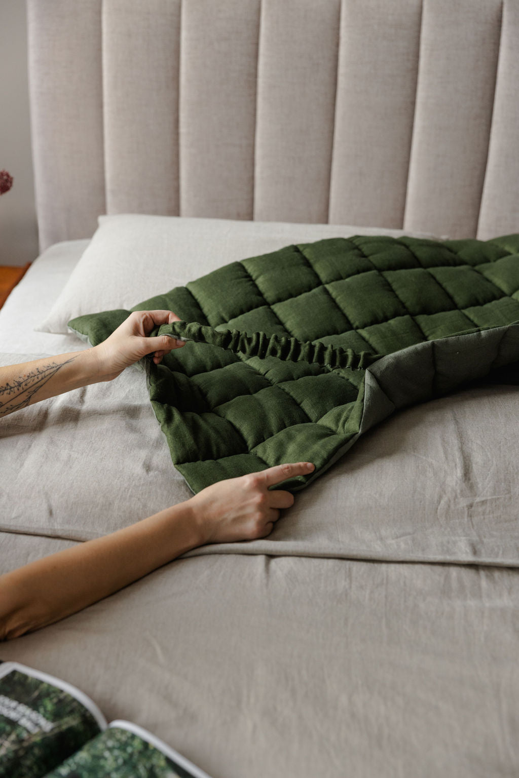 Person arranging a green woven blanket on a bed.