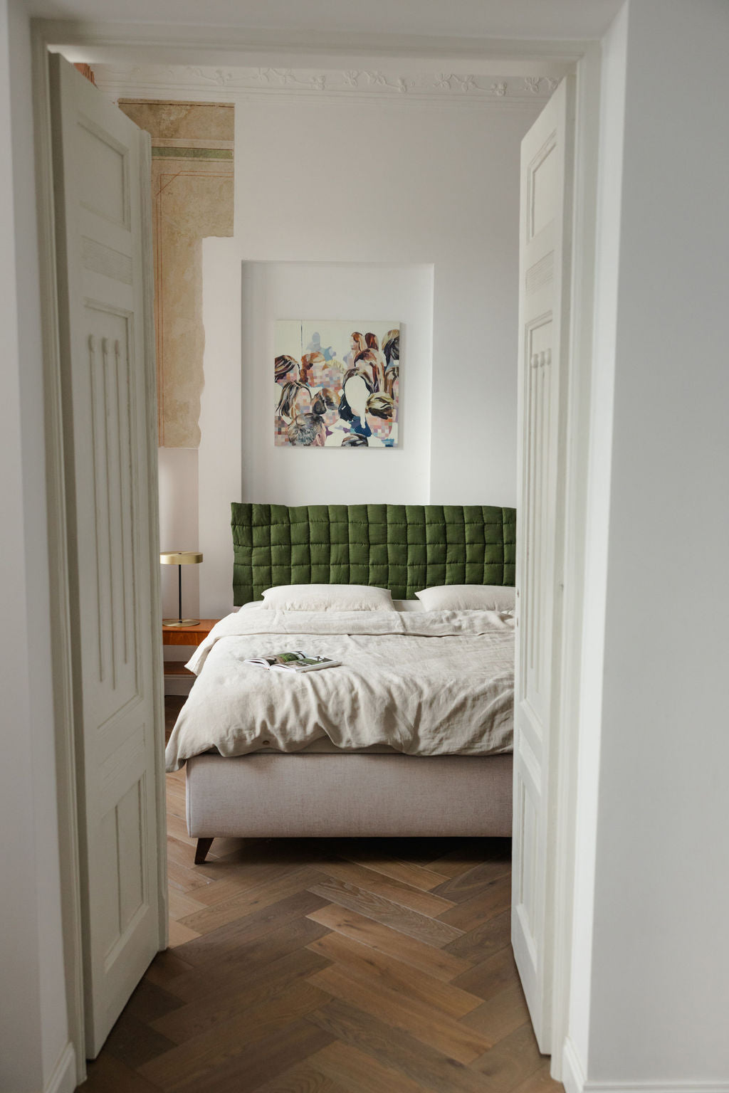 Bedroom with green upholstered headboard and artwork on wall