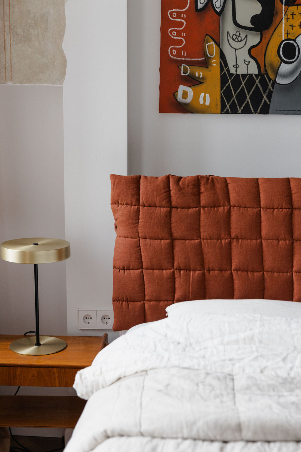 Bedroom with orange quilted headboard, white bedding, and a lamp on a nightstand.
