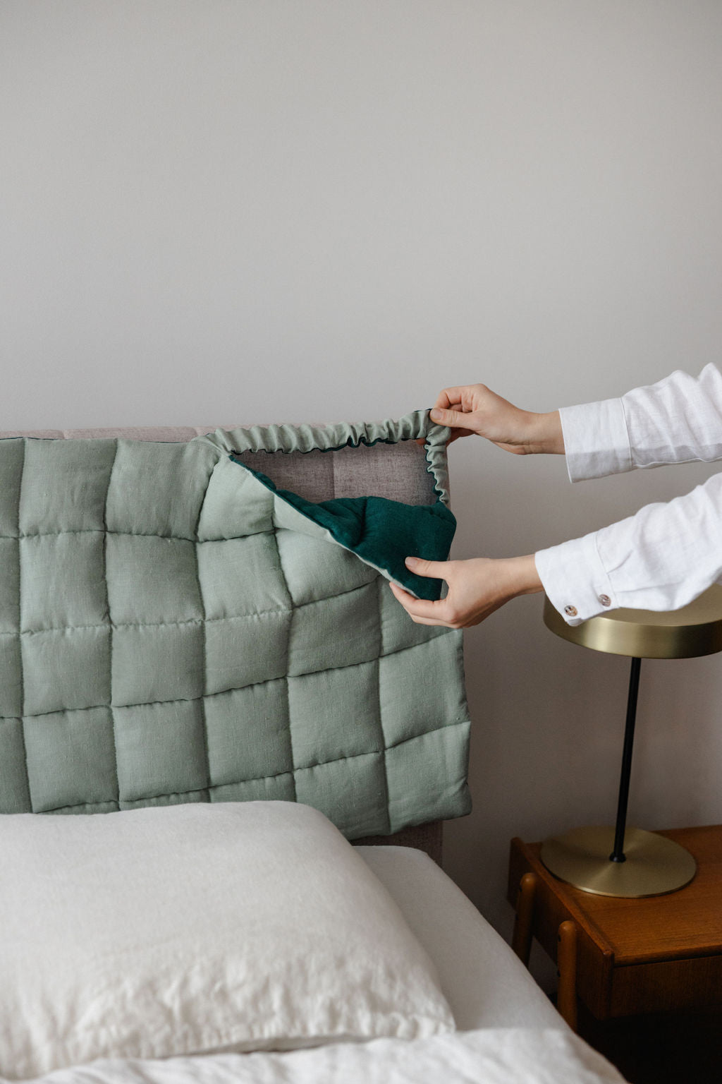 Person adjusting a green pillow on a bed with a neutral background
