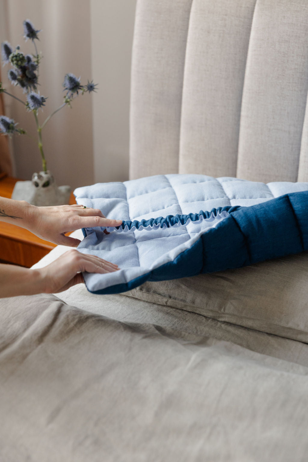 Person folding a blue quilt on a bed with a neutral background