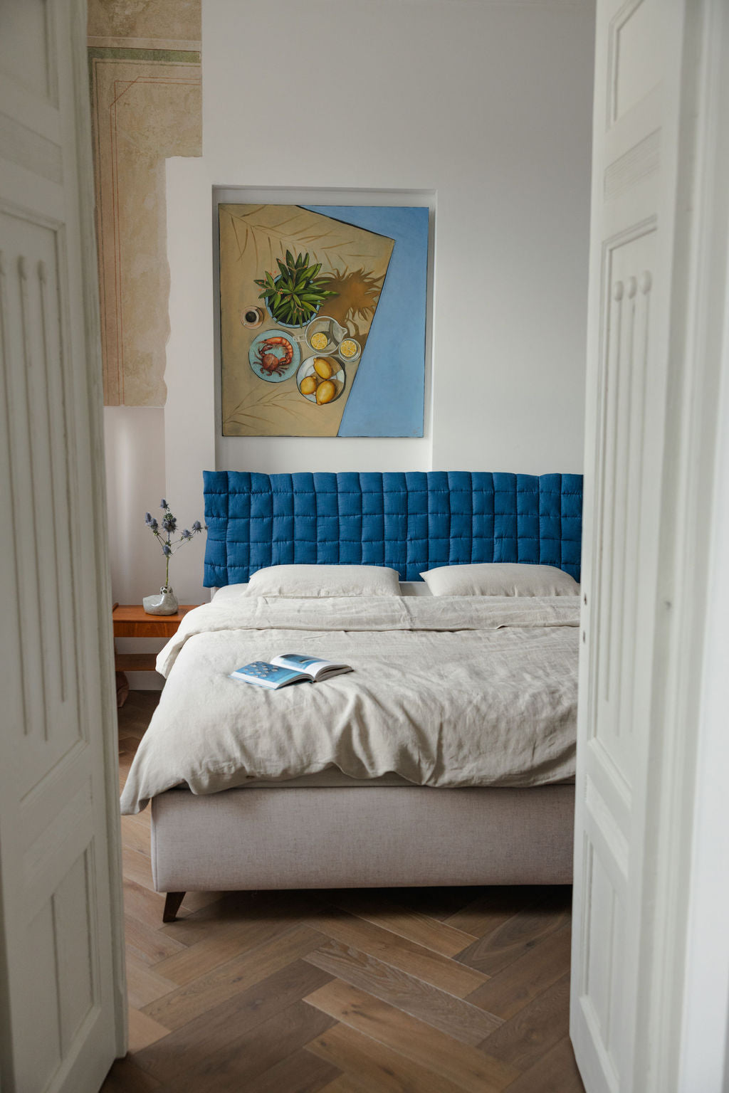 Bedroom with a blue headboard and a painting on the wall.