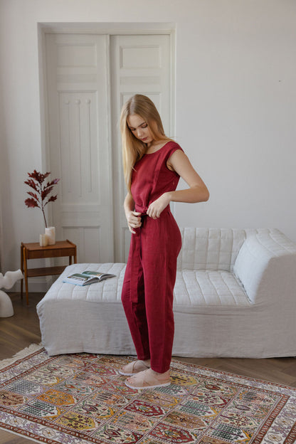 Woman in a red jumpsuit standing in a room with a white sofa and decorative rug.