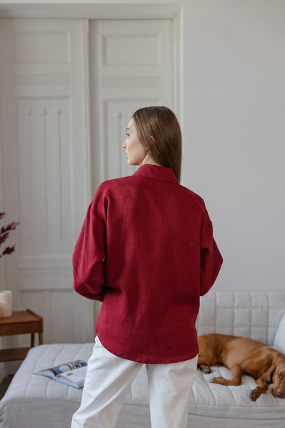 Person wearing a red shirt standing in a room with a dog on a bed.