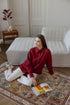 Woman in a red shirt sitting on a patterned rug with an open book