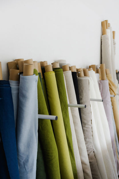 Rolls of fabric in various colors on a rack against a white wall

