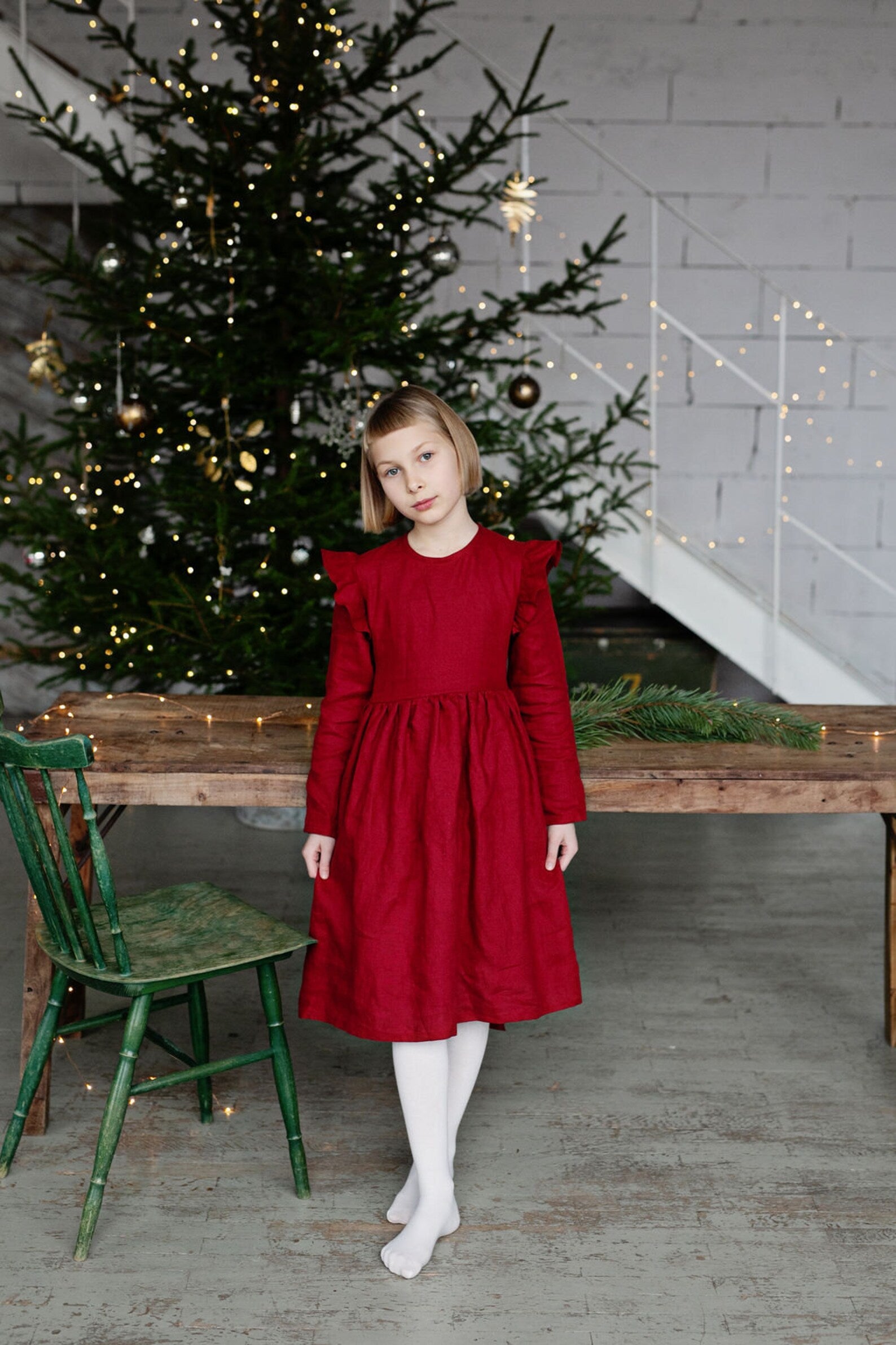 Girl in a red linen dress sitting in front of a decorated Christmas tree.
