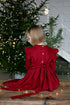 Girl in a red linen dress sitting in front of a decorated Christmas tree.

