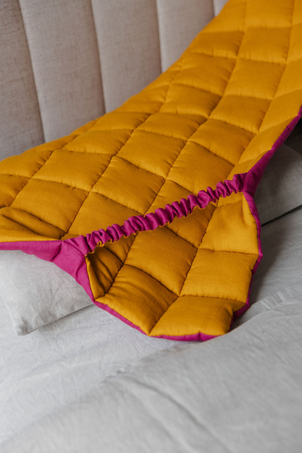 Yellow headboard cover with pink trim on a bed
