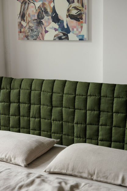 Green quilted headboard with pillows and a colorful abstract painting on the wall.