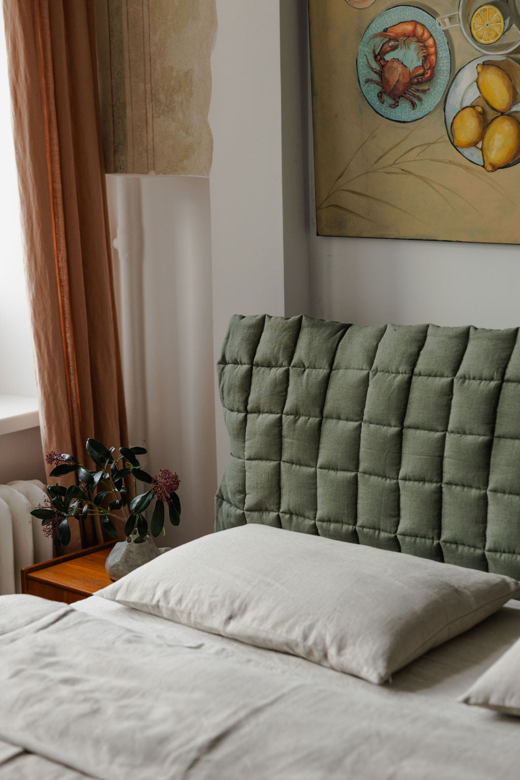 Bedroom with a green quilted headboard and light bedding, featuring a painting on the wall.