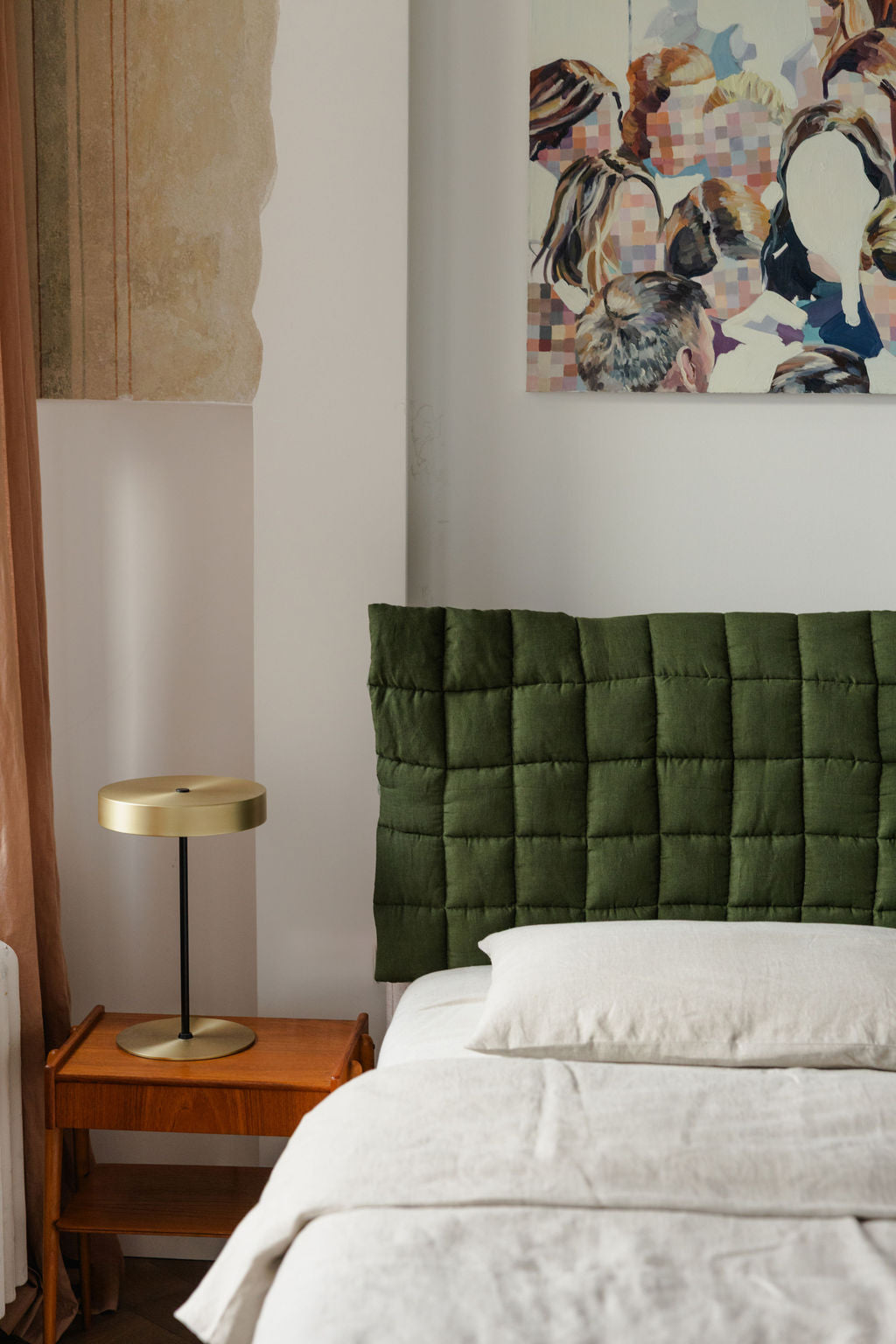 Bedroom with green upholstered headboard, white bedding, and a gold lamp on a wooden nightstand.