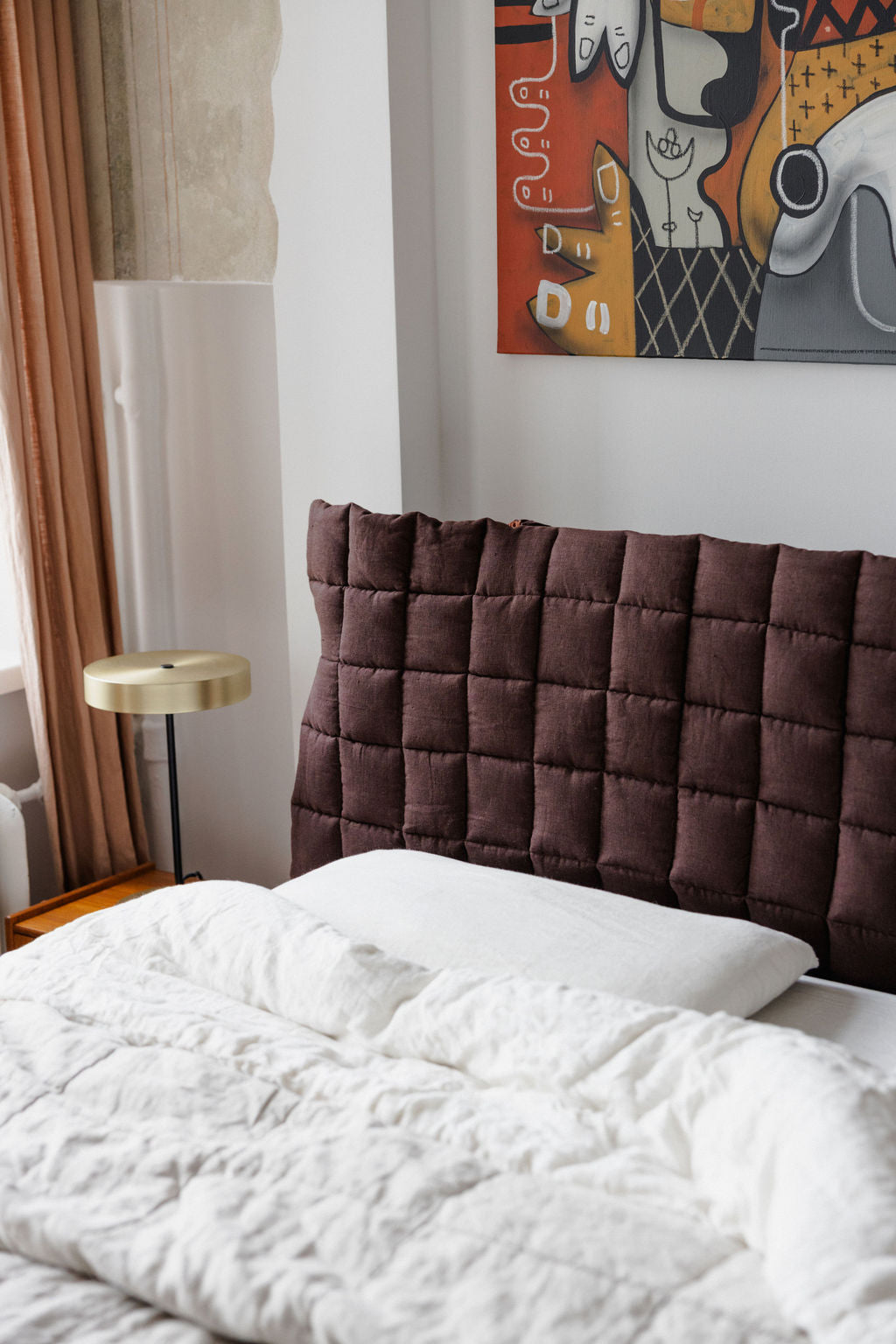 Bedroom with a brown quilted headboard and white bedding, featuring a colorful abstract painting on the wall.