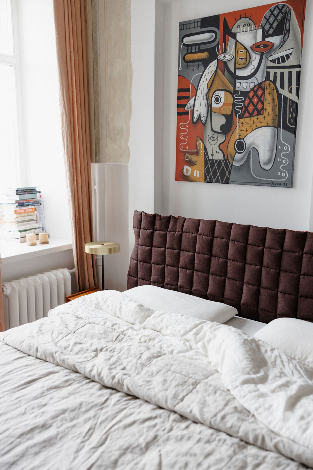 Bedroom with a brown quilted headboard, white bedding, and abstract artwork on the wall.