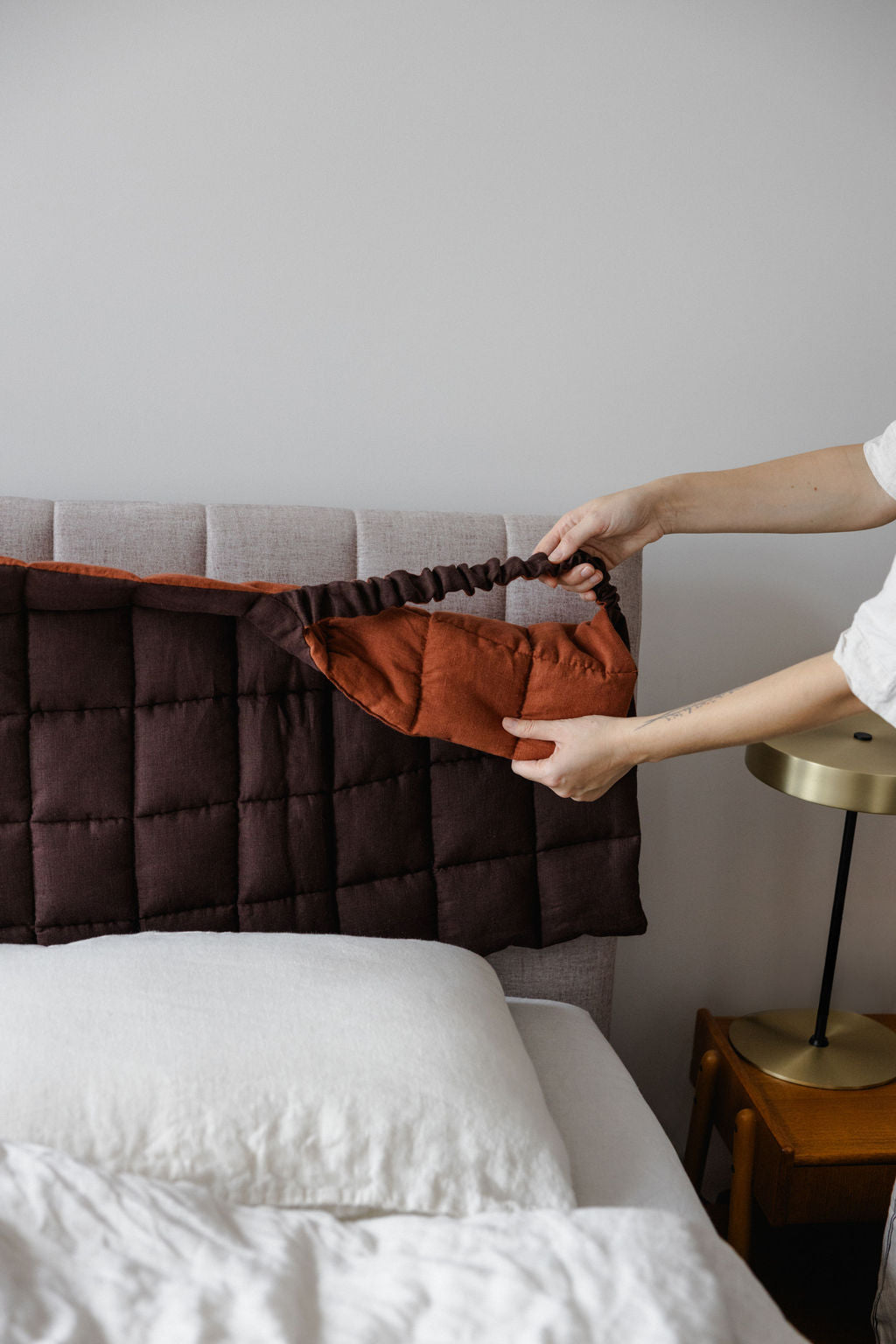 Person adjusting a pillow on a bed with a neutral background