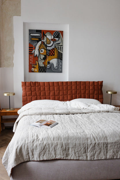 Bedroom with a red quilted headboard and abstract art on the wall.