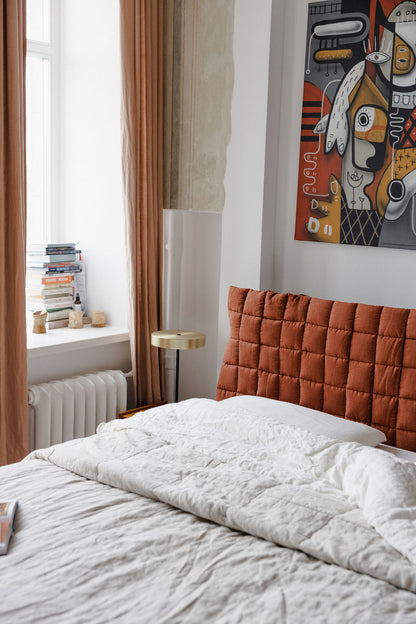 Bedroom with a bed featuring a rust-colored quilted headboard, white bedding, and a colorful abstract painting on the wall.