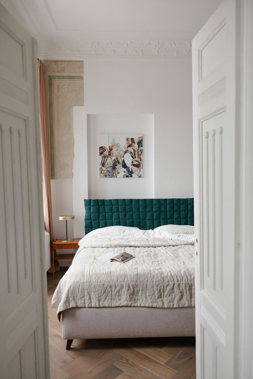 Bedroom with a green headboard and white bedding, featuring a painting on the wall.