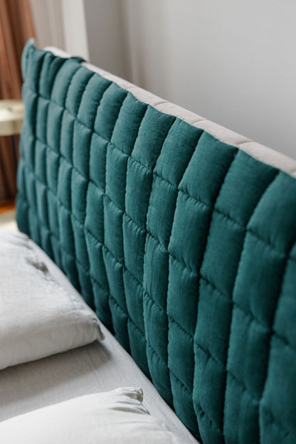 Teal quilted headboard on a bed with white pillows