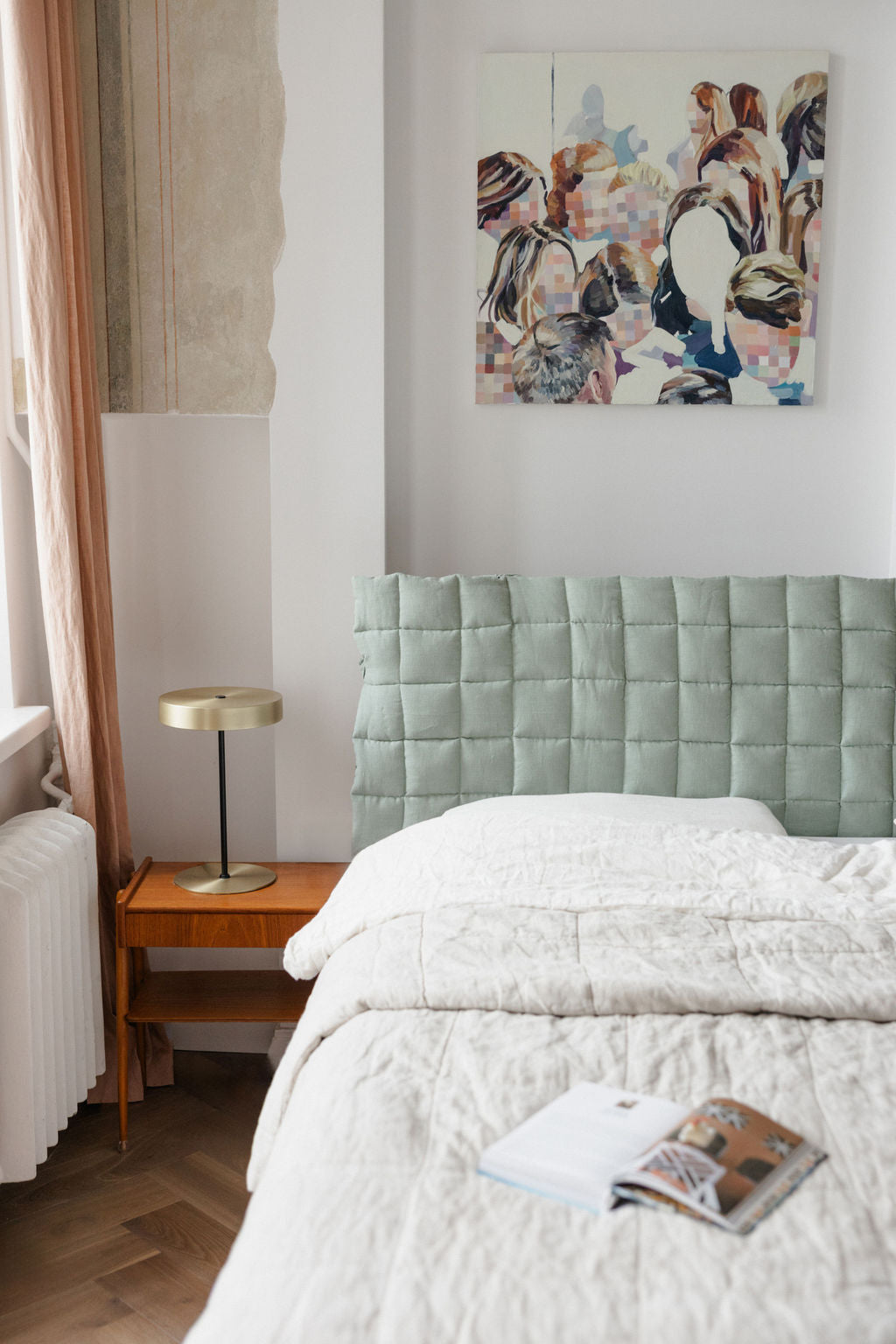 Bedroom with a light green upholstered headboard and a colorful painting on the wall.