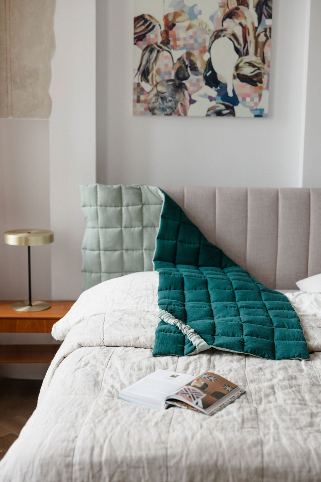 Bedroom with a bed featuring a green quilt, a lamp, and a painting on the wall.