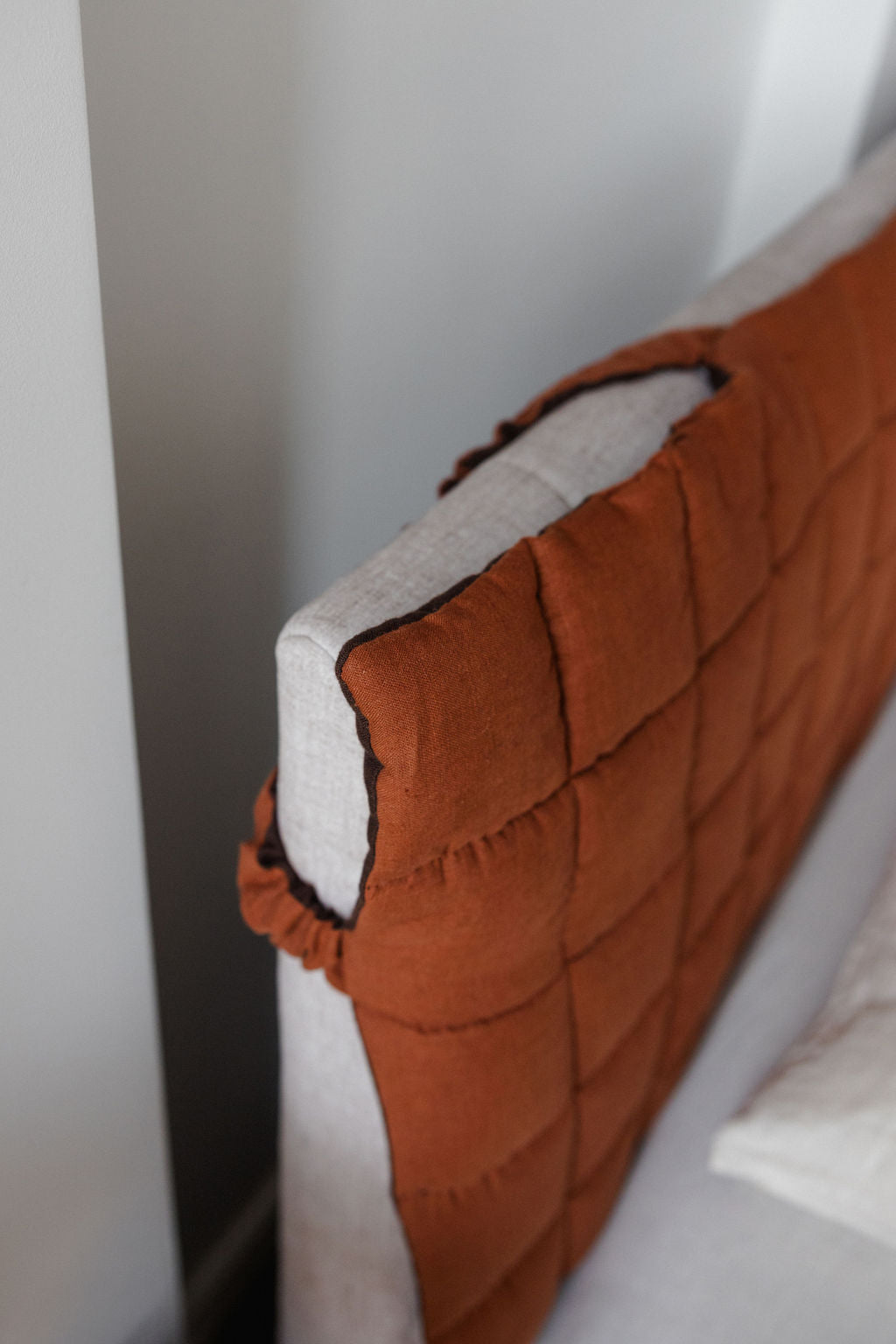 Close-up of a brown quilted headboard against a white wall.