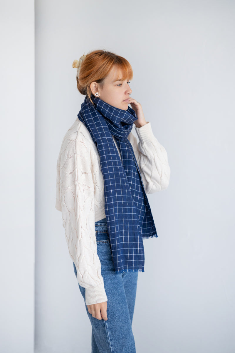 Person wearing blue linen checkered scarf against a plain background
