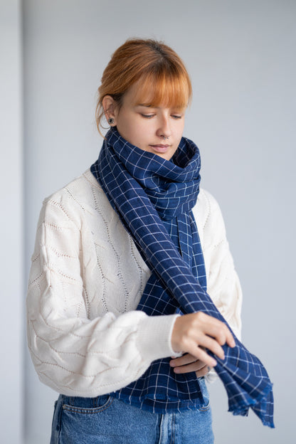 Woman wearing a blue checkered linen scarf and white sweater against a gray background