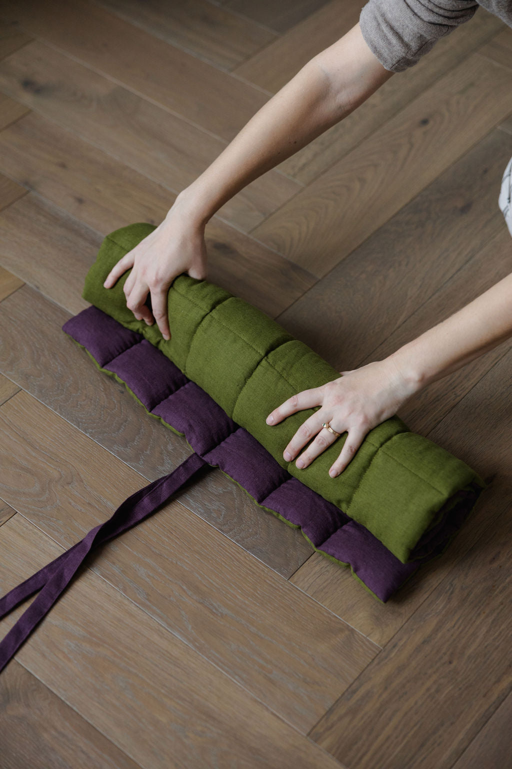 Person rolling up a green mat with purple straps on a wooden floor