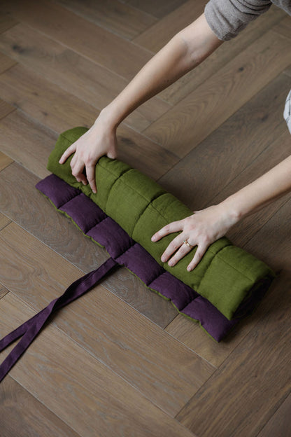 Person rolling up a green mat with purple straps on a wooden floor