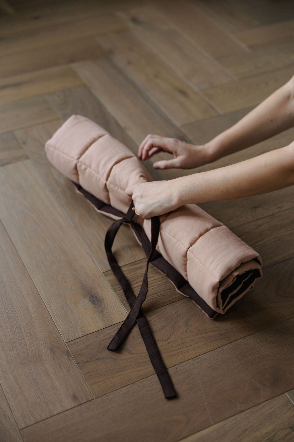 Person holding a rolled-up pink blanket on a wooden floor