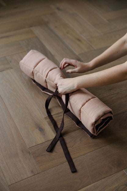 Person holding a rolled-up pink blanket on a wooden floor